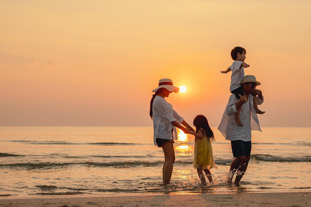 Family playing by the ocean at sunset
